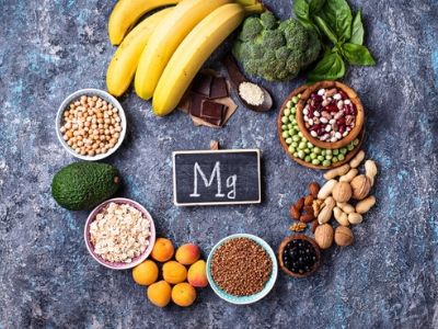 Formula chimica del magnesio (Mg) scritta in una lavagna al centro di un cerchio formato da alimenti che sono ricchi di magnesio, come banane, cioccolato fondente ecc..