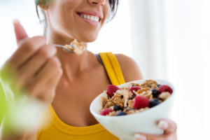 Beautiful young woman eating cereals and fruits at home.